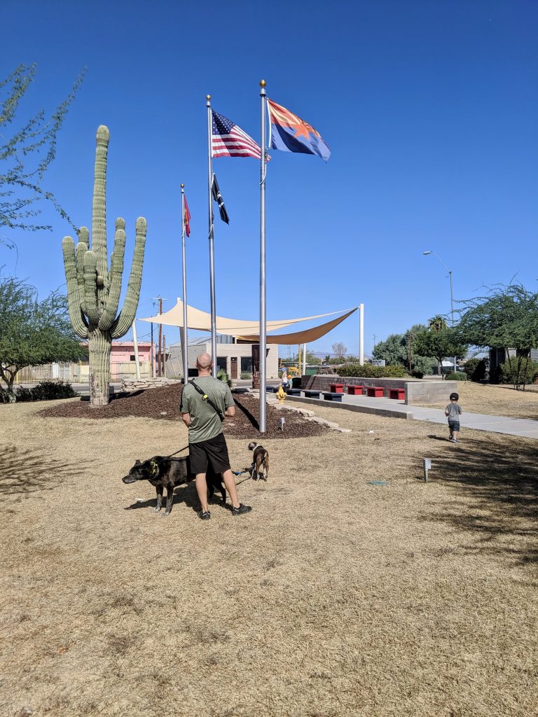 Full-time RV family visiting a patriotic memorial park, walking with kids and dogs beneath American flags