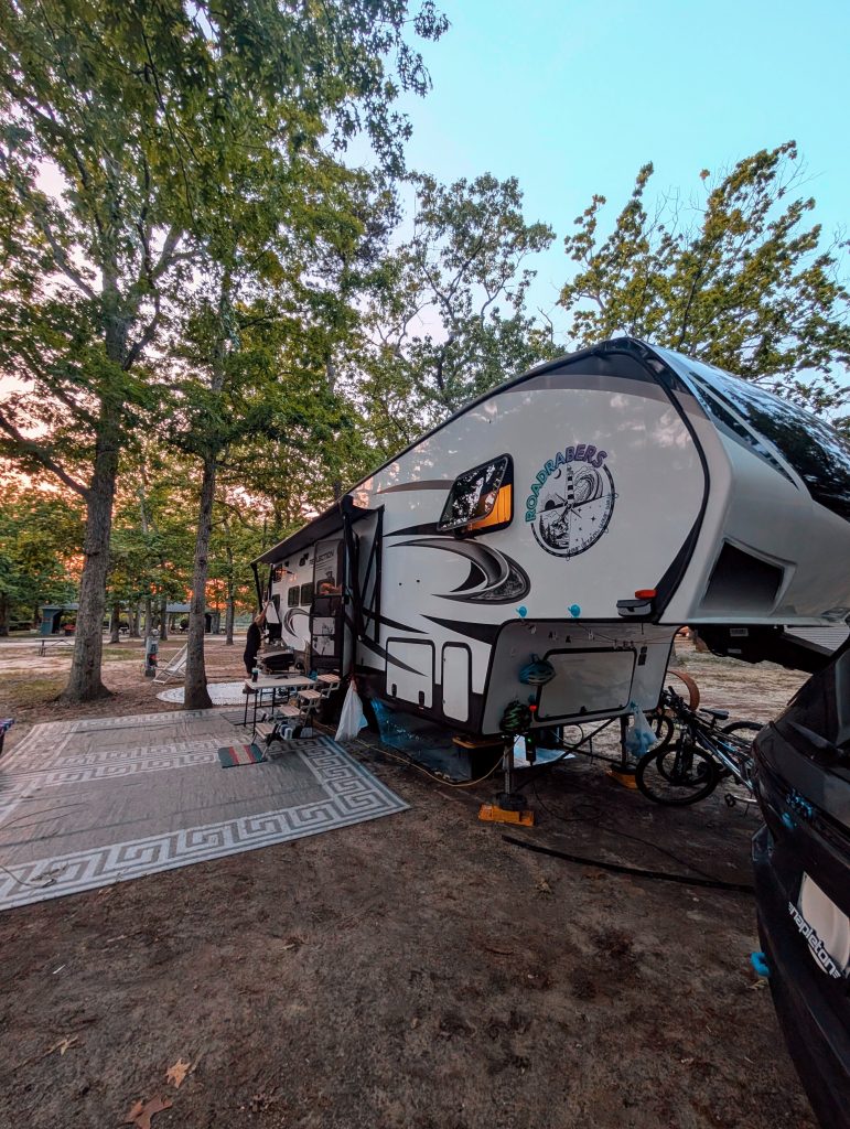 Our RV parked at Lake and Shore campground in New Jersey under tall trees, set up with rugs and outdoor gear as part of our Thousand Trails stay near Philadelphia.